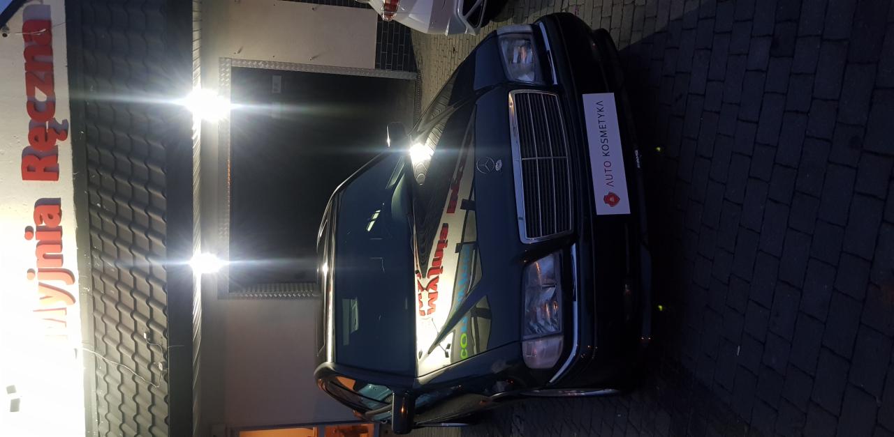 Czarny Mercedes W124 po zabiegach auto kosmetyki, zaparkowany przed budynkiem myjni ręcznej z widocznym szyldem.