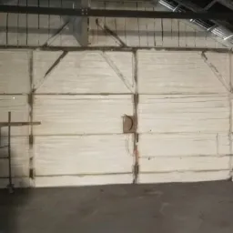 Wnętrze budynku z drewnianą konstrukcją dachu, ściany pokryte białą, grubą warstwą izolacji natryskowej. Widoczny fragment rusztowania z lewej strony.