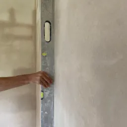 Sprawdzanie pionu ściany za pomocą poziomicy, widoczne ślady po szpachlowaniu.