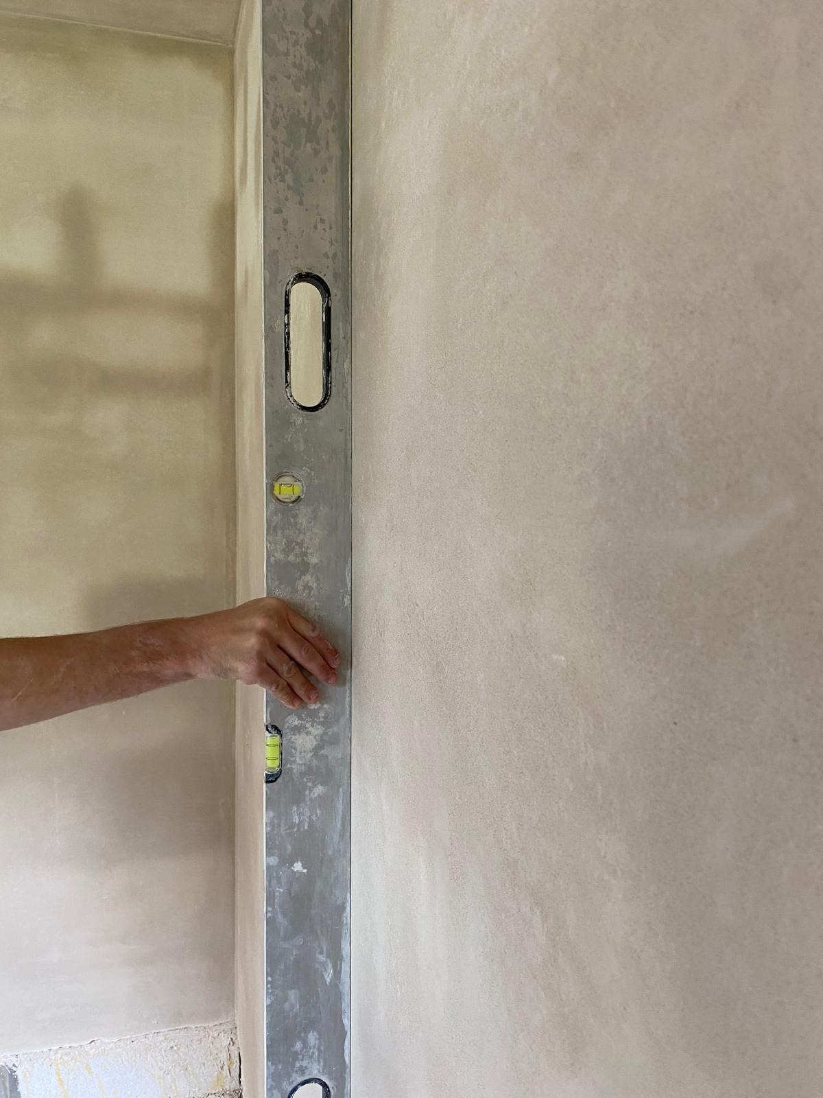 Sprawdzanie pionu ściany za pomocą poziomicy, widoczne ślady po szpachlowaniu.