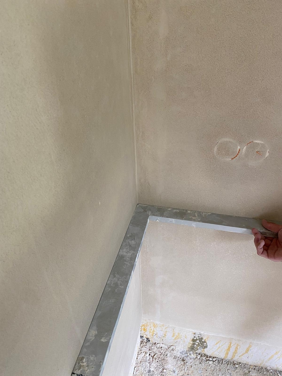 Przygotowanie narożnika ściany do wykończenia, widoczny profil aluminiowy i ślady po szpachlowaniu, w tle puszki elektryczne.