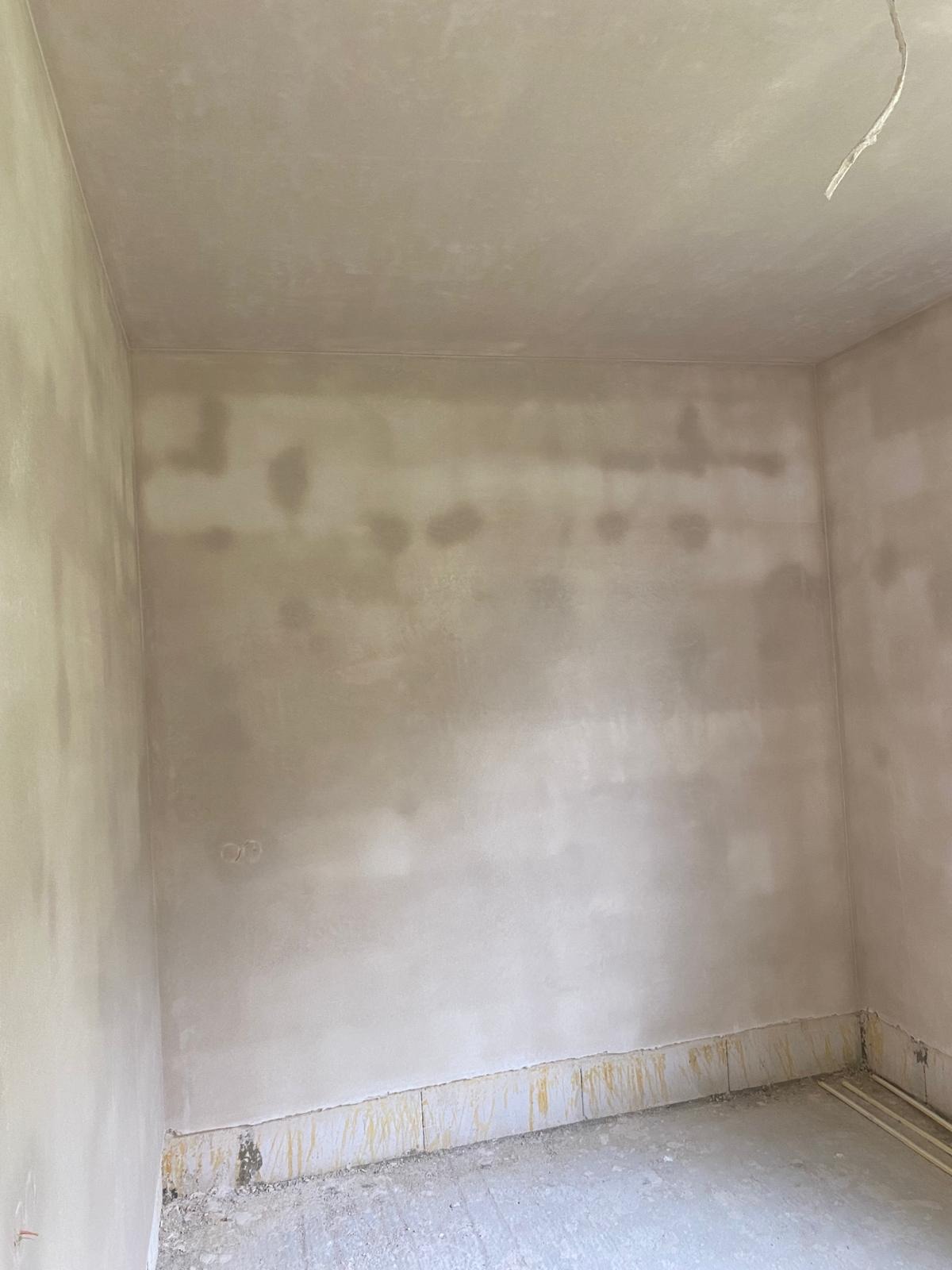 Pokój po szpachlowaniu ścian i sufitu, widoczne niedoskonałości i ślady po łataniu, przygotowany do malowania, z widocznymi przewodami elektrycznymi wystającymi ze ściany.