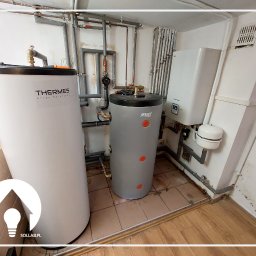 Sollab - Dwa zbiorniki akumulacyjne ciepła (biały i szary) w kotłowni, obok wiszący na ścianie biały piec gazowy z wyświetlaczem, widoczne rury instalacji grzewczej.