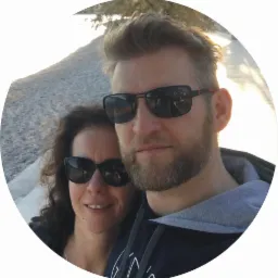 Zdjęcie portretowe pary w okularach przeciwsłonecznych, ubranych w odzież z potencjalnym miejscem na nadruk, na tle krajobrazu w słoneczny dzień.