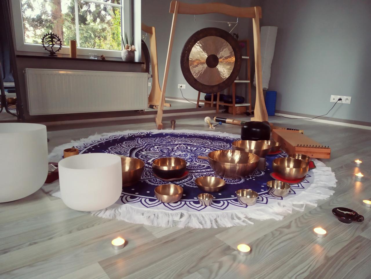 Aranżacja do terapii dźwiękiem: gong, kryształowe i metalowe misy, kotoński, świece na podłodze z paneli, okrągły dywan z frędzlami, widok z niskiego kąta.