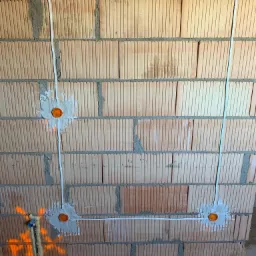 Ściana z cegły ceramicznej z widocznymi, częściowo zamurowanymi puszkami instalacyjnymi i przewodami elektrycznymi, pianka montażowa w dolnej części ściany.