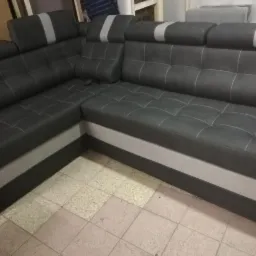 Ciemnoszary narożnik z funkcją relax, pikowane siedzisko i oparcie, jasnoszary pas na dole i na zagłówkach, widoczne szwy w kolorze ecru.