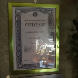 Certyfikat doradcy podatkowego Haliny Klekot w złotej ramie, wiszący na ścianie z kamienną fakturą, pod nim tabliczka informacyjna z danymi doradcy.