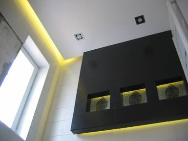 Nowoczesna łazienka z czarną zabudową i podświetlanymi niszami z dekoracyjnymi motywami liści, oświetlenie punktowe i taśma LED przy suficie, widok z dołu.