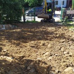 USŁUGI OGÓLNOBUDOWLANE KOPARECZKA Łukasz Luszowski - Żółta mini koparka Yanmar na wyrównanym terenie budowy, widoczne ogrodzenie i zabudowa jednorodzinna w tle.