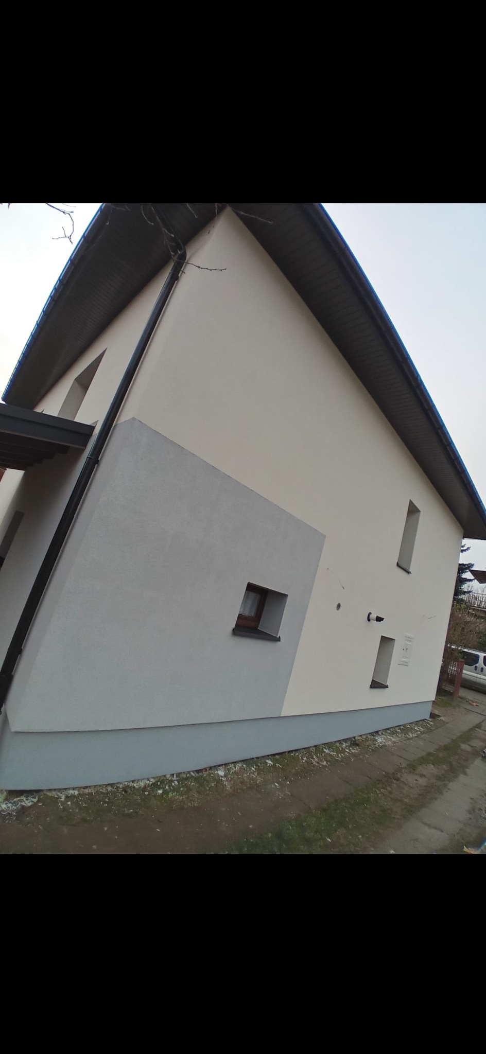 Dwukondygnacyjny dom z elewacją w odcieniach szarości i bieli, widok z dołu, rynna i okna z ciemnymi ramami.