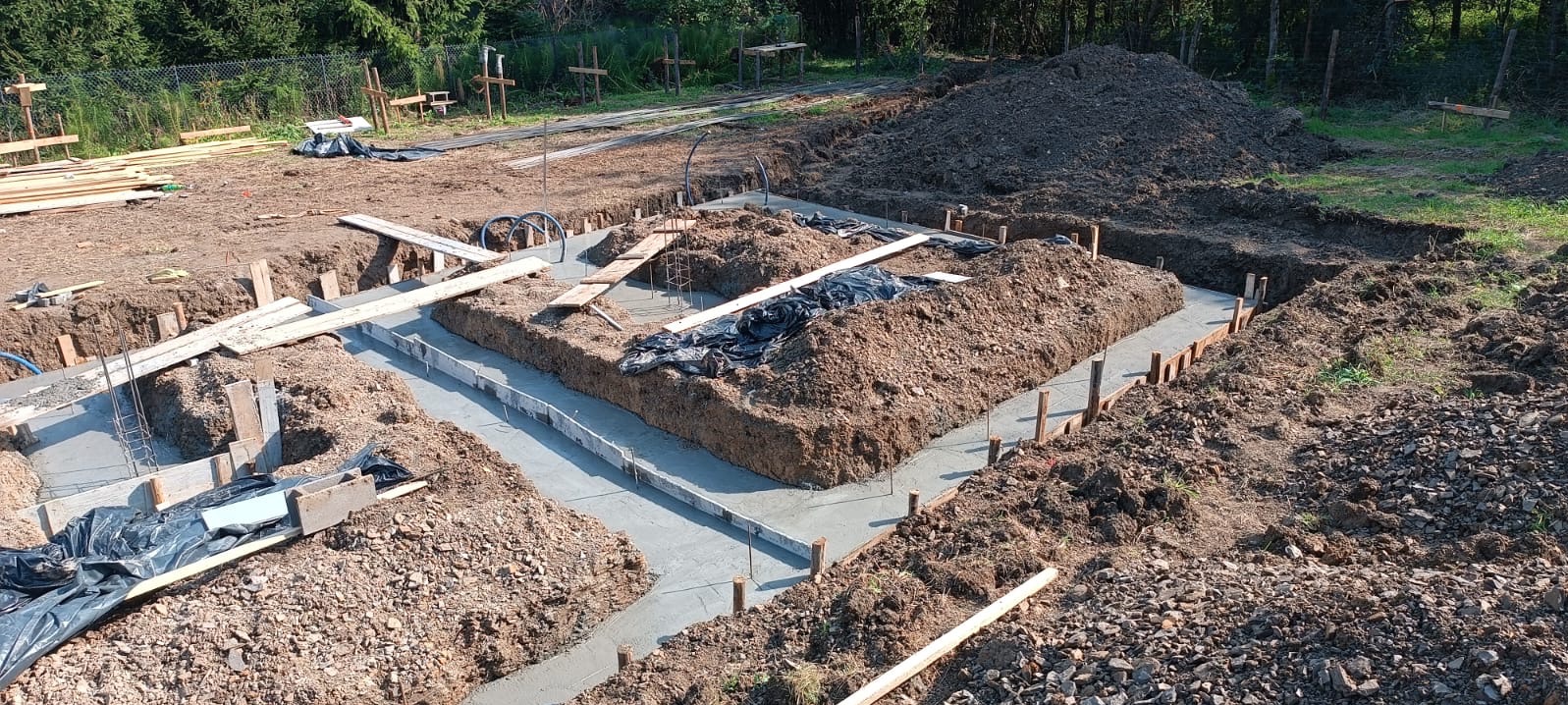 Wylane fundamenty domu jednorodzinnego z widocznym szalunkiem i wykopami ziemnymi, przygotowane do dalszych prac budowlanych.