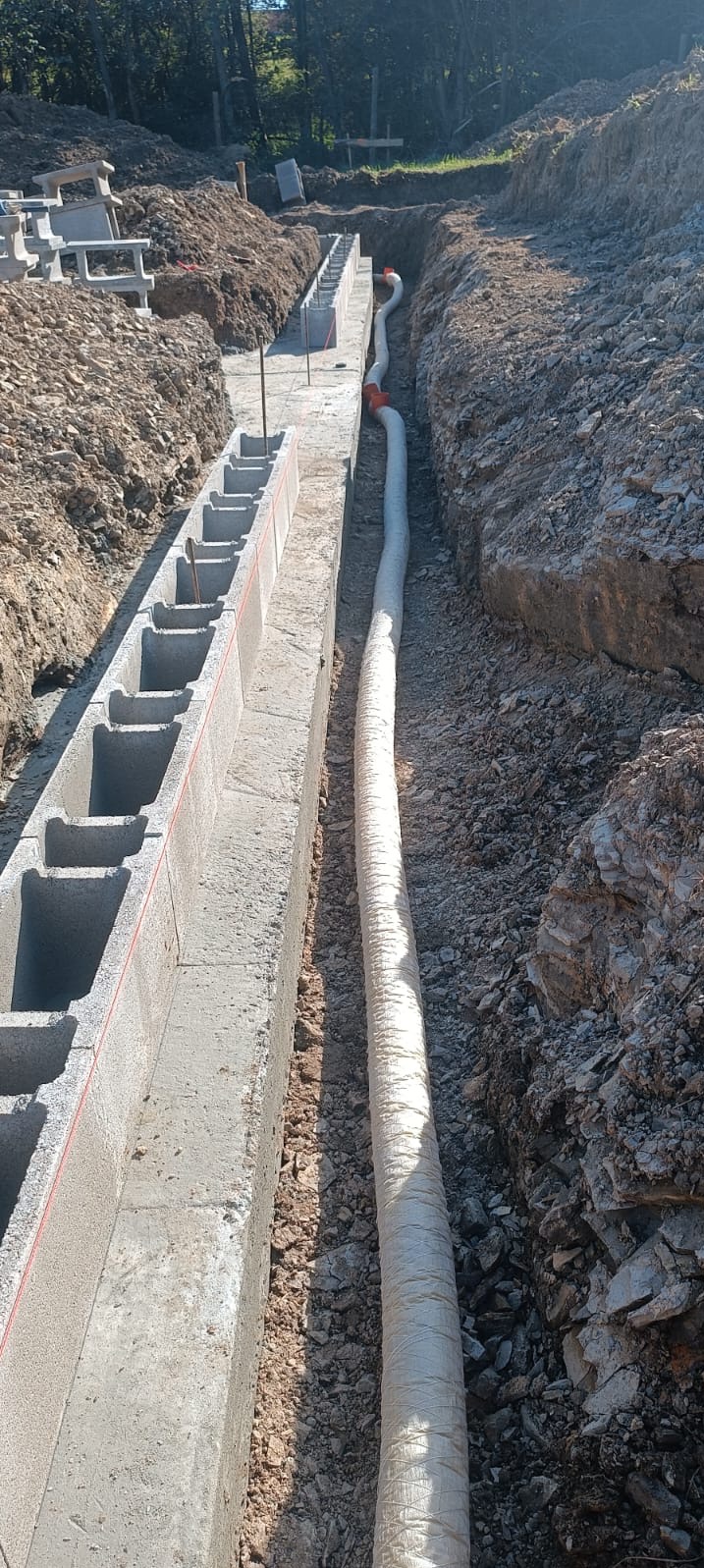 Fundament z betonowych pustaków i rura drenarska w wykopie, widok z góry.