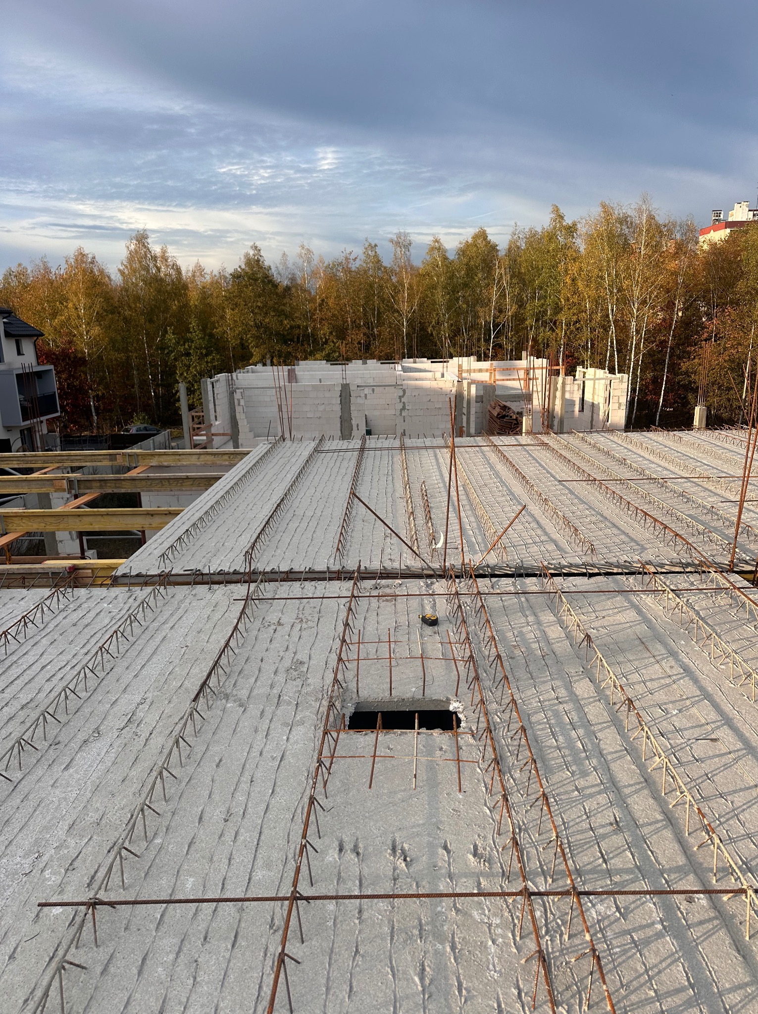 Żelbetowy strop Teriva w trakcie budowy domu, widoczne zbrojenie i otwór instalacyjny, w tle ściany z betonu komórkowego i jesienne drzewa.