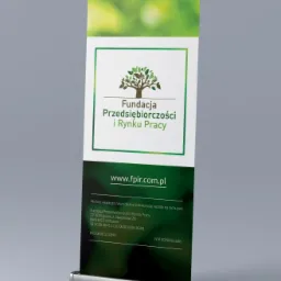 Roll-up reklamowy Fundacji Przedsiębiorczości i Rynku Pracy z logo drzewa, adresem strony internetowej i danymi kontaktowymi, ustawiony na szarym tle.