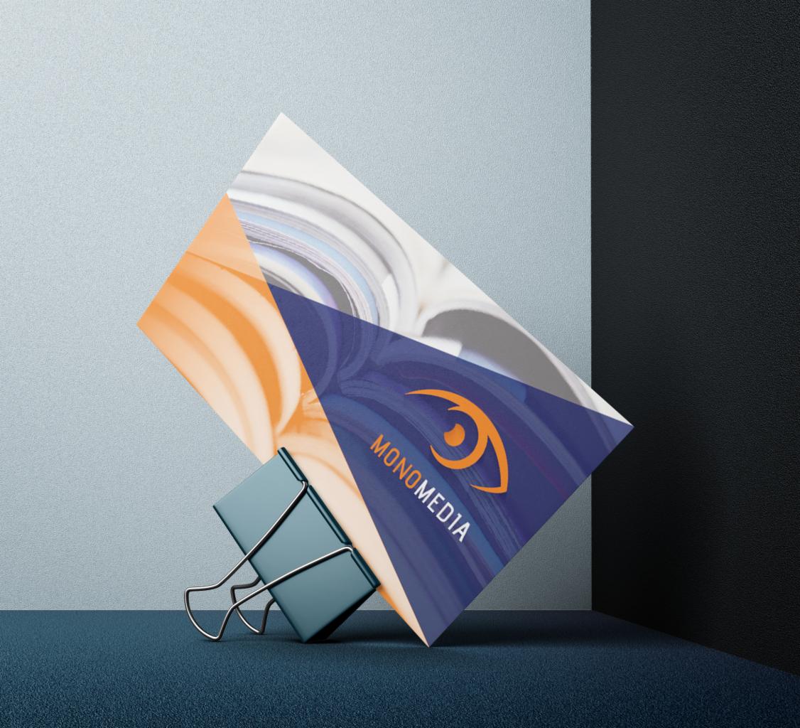 Stylizowana wizytówka Monomedia z logo oka, przypięta klipsem na teksturowanym, niebieskim tle z gradientem.