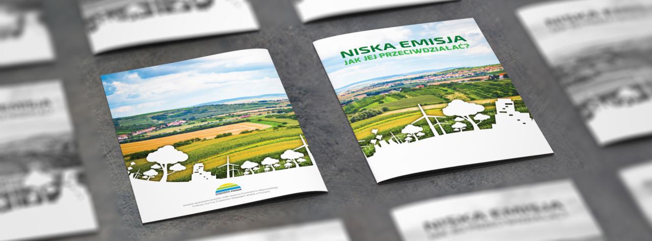 Stos ulotek na szarym tle, na pierwszym planie dwie otwarte ulotki z ilustracjami krajobrazu i tekstem 'Niska Emisja. Jak jej przeciwdziałać?'