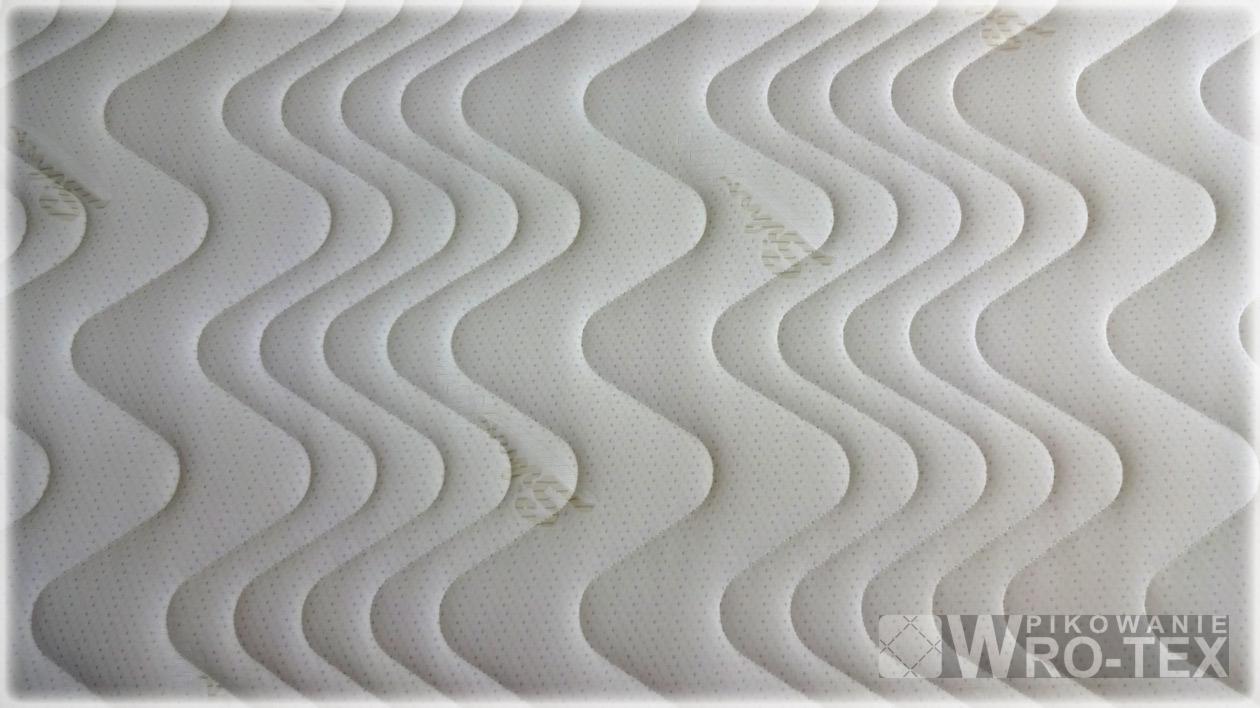 Pikowana, biała tkanina materaca z falistym wzorem, widoczne logo firmy WRO-TEX w prawym dolnym rogu.