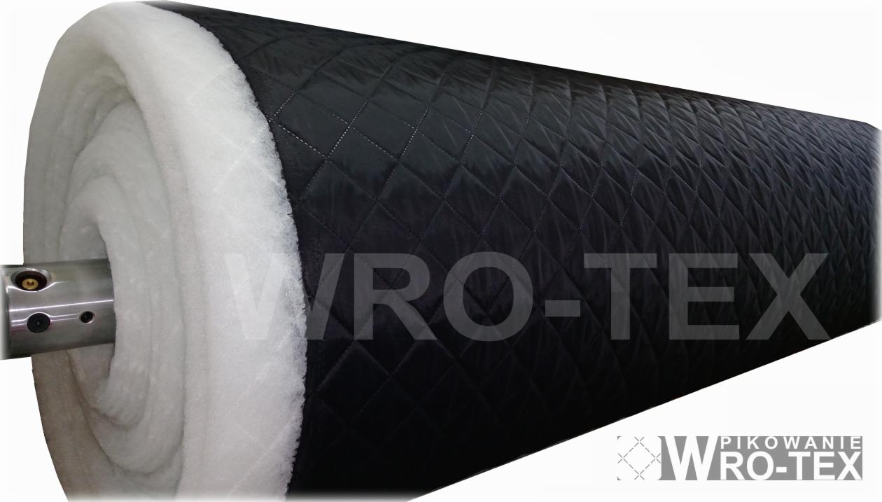 Rolka czarnej pikowanej tkaniny z białym wypełnieniem, nawinięta na metalowy wałek.
