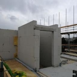 Malta - Wznoszenie ścian z bloczków na budowie domu, widoczne pręty zbrojeniowe i rusztowania w tle, pochmurne niebo.