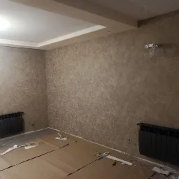 Pokój we Wrocławiu po nałożeniu dekoracyjnej gładzi w odcieniach beżu, z widocznymi grzejnikami i przygotowanym podłożem pod panele.