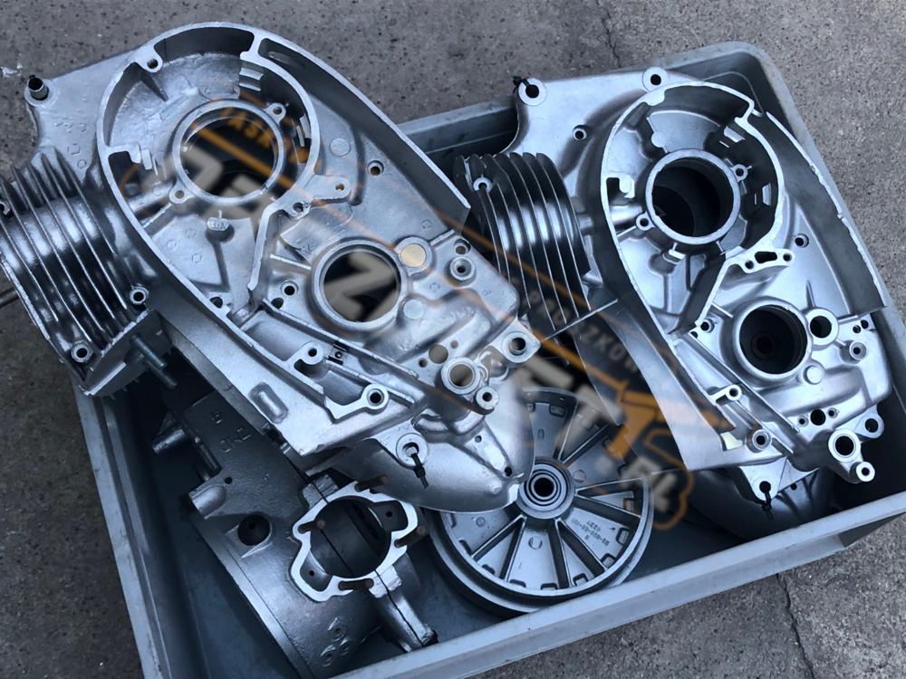 Metalowe elementy silnika motocyklowego w szarej kuwecie, po obróbce strumieniowo-ściernej, przygotowane do dalszej renowacji.