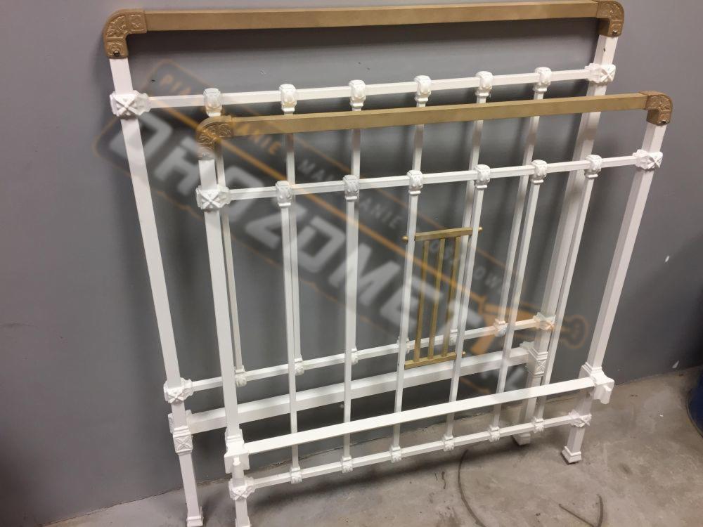 Biała, metalowa rama łóżka z dekoracyjnymi elementami, po renowacji, z widocznymi fragmentami oryginalnego, złotego koloru.