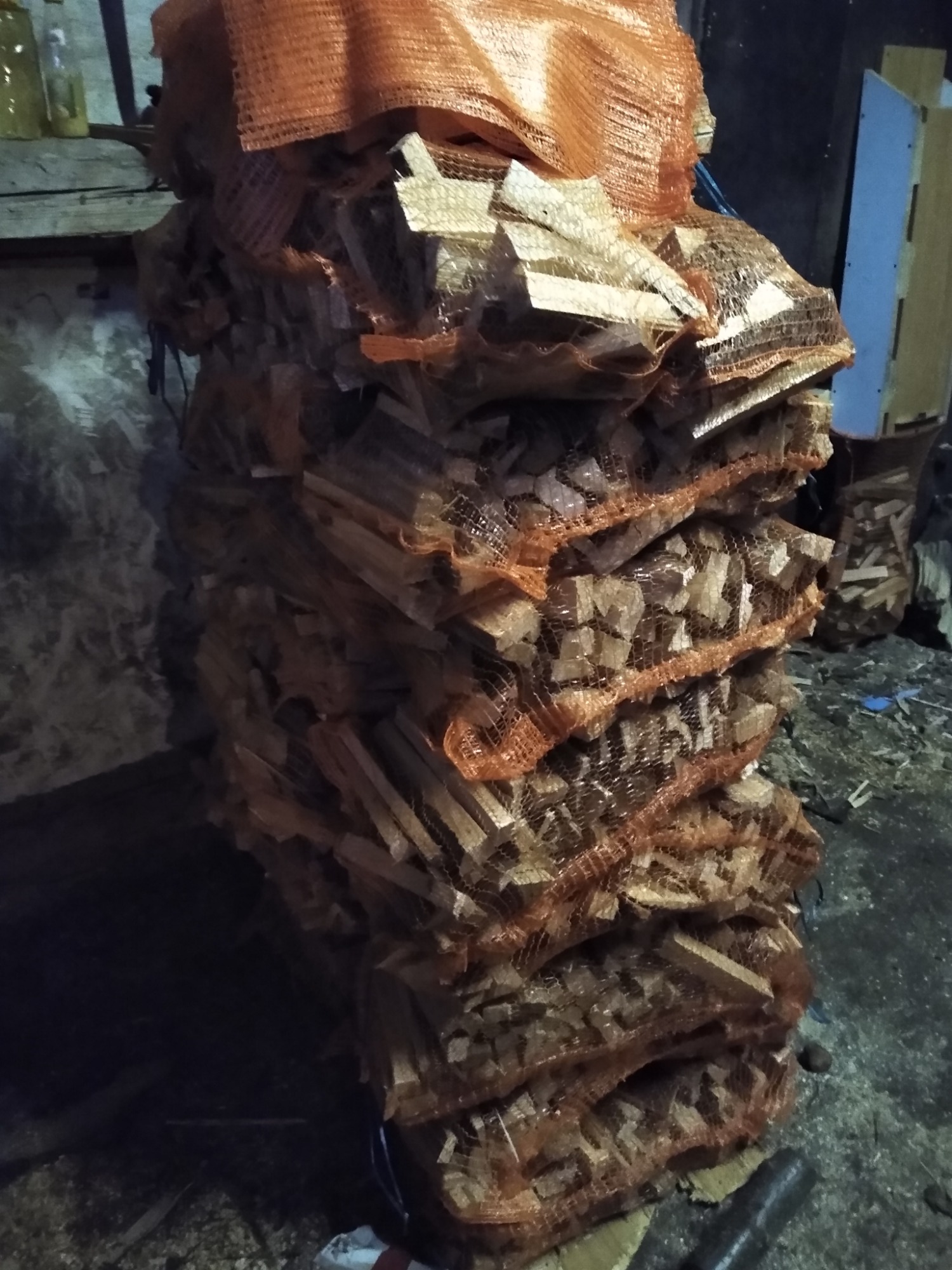 Stos worków z pociętym drewnem ułożonych jeden na drugim, widoczne kawałki drewna przez pomarańczową siatkę worków.