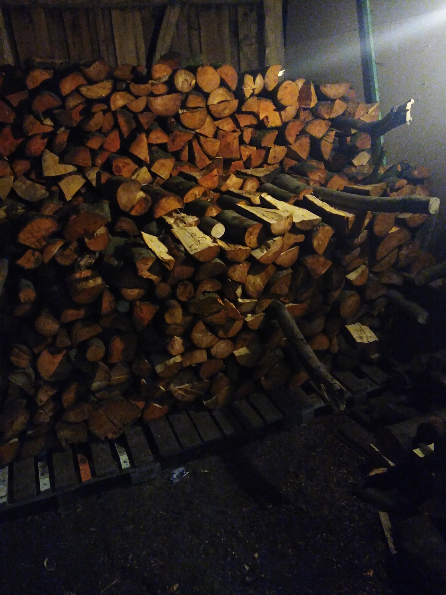 Stos pociętego drewna ułożonego na palecie w Starych Bogaczowicach, widoczne ciemne tło i słabe oświetlenie.