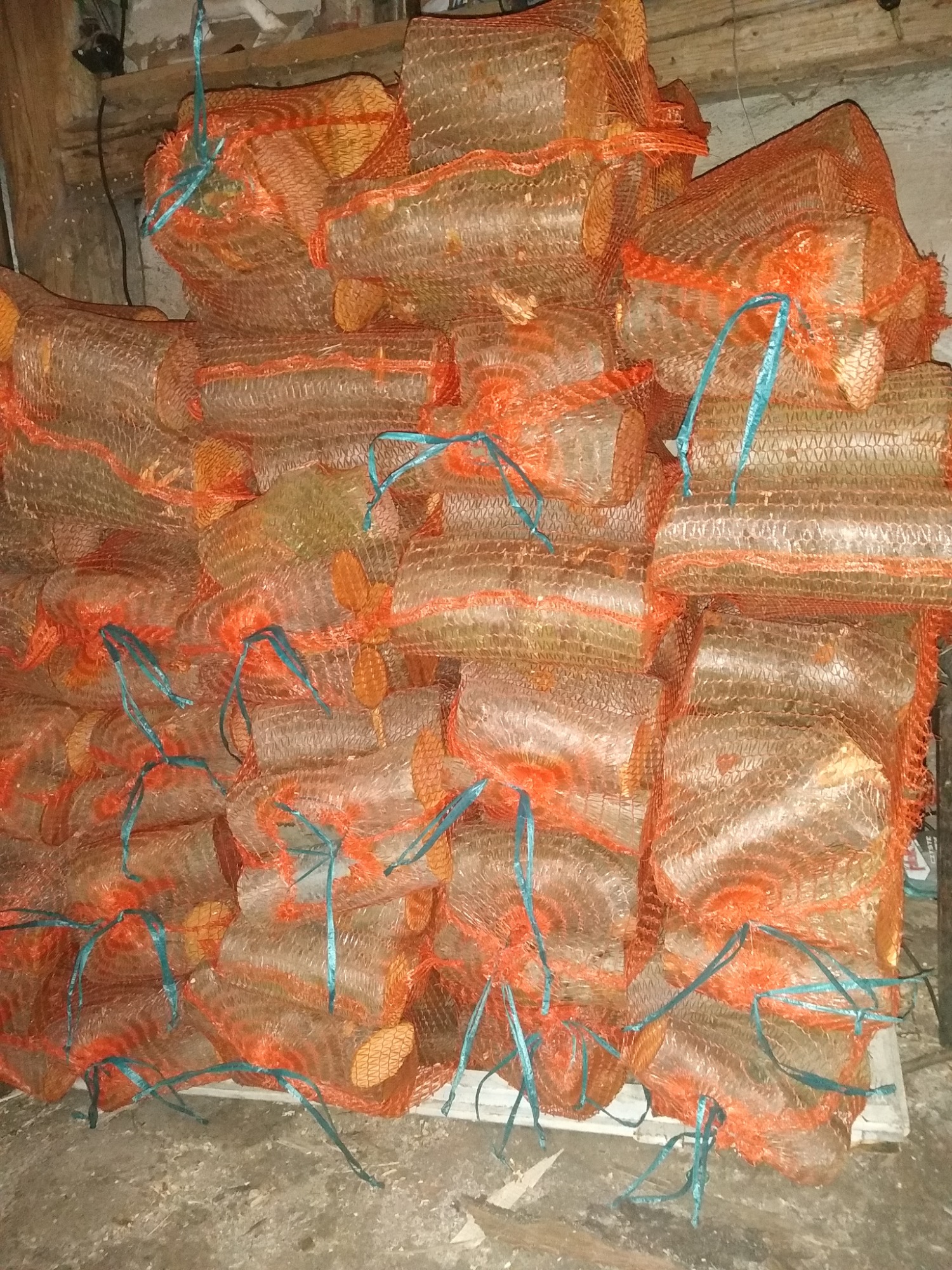 Stos worków wypełnionych pociętym drewnem, zabezpieczonych niebieskim sznurkiem, ułożonych na palecie w magazynie.