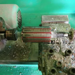 Wirnik silnika elektrycznego zamocowany w tokarce, widoczne wióry po obróbce, czerwone paski na wirniku.