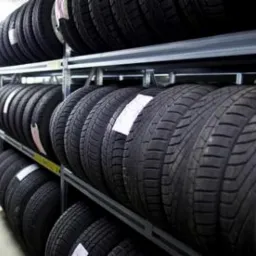 Rząd opon na metalowych regałach w magazynie, widoczne białe etykiety na niektórych oponach.