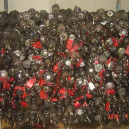 Metalowa klatka wypełniona po brzegi używanymi p&oacute;łosiami samochodowymi z czerwonymi etykietami, widoczne ślady użytkowania i r&oacute;żnice w modelach.