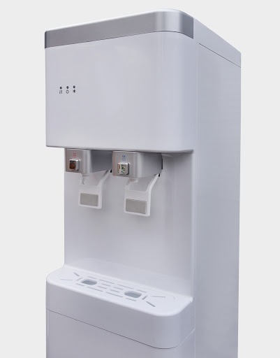 Nowoczesny, biały dystrybutor wody z dwoma kranami, z widocznymi diodami sygnalizacyjnymi na górze obudowy, na jednolitym, jasnym tle.