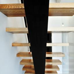 Pracownia Snycerska u Pawła - Minimalistyczne schody z drewnianymi stopniami i czarną, metalową konstrukcją nośną, widok z dołu, nowoczesne wnętrze.
