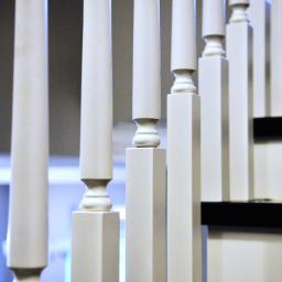 Pracownia Snycerska u Pawła - Białe, lakierowane słupki balustrady przy czarno-białych stopniach schodów, widok z bliska, z delikatnym rozmyciem tła.