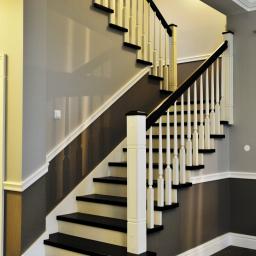 Pracownia Snycerska u Pawła - Eleganckie schody z czarnymi stopniami i białymi balustradami w domu w Wierzchowie, wykończone listwami przypodłogowymi i sztukaterią.