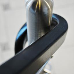 Pracownia Snycerska u Pawła - Szczegółowe ujęcie fragmentu balustrady ze stali nierdzewnej z czarną poręczą, widoczne refleksy światła na polerowanej powierzchni.