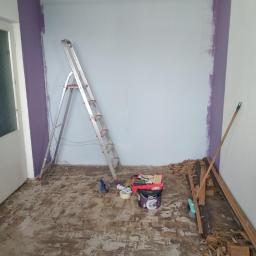 FHU Dariusz Bojaś - Pokój w trakcie przygotowania do malowania: ściany częściowo pomalowane na fioletowo, drabina aluminiowa, wiadro z farbą Dulux, resztki starej podłogi na podłodze.