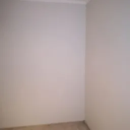 Pomalowany na szaro róg pokoju z listwą przypodłogową i wykończeniową, widoczne panele podłogowe imitujące drewno.