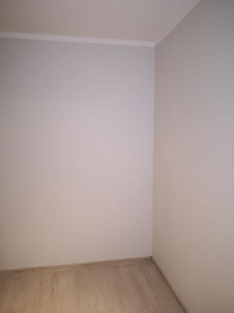 Pomalowany na szaro róg pokoju z listwą przypodłogową i wykończeniową, widoczne panele podłogowe imitujące drewno.