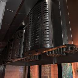 Niko-Tech - Szereg przemysłowych okapów wentylacyjnych ze stali nierdzewnej, zamontowanych w restauracji, widok od dołu, z widoczną tablicą menu w tle.