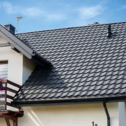 Dom jednorodzinny z szarą blachą trapezową w Tomaszowie Lubelskim, widok z boku, balkon z kwiatami.