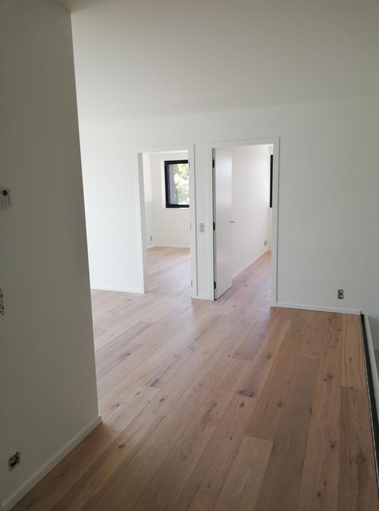 Jasne, drewniane podłogi w nowym, minimalistycznym wnętrzu z białymi ścianami i otwartymi drzwiami.