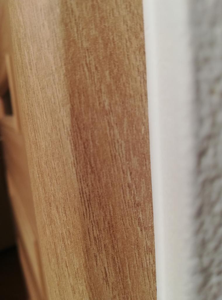 Fragment ściany z widoczną strukturą drewna na okładzinie i połączeniem z gładką, białą powierzchnią.