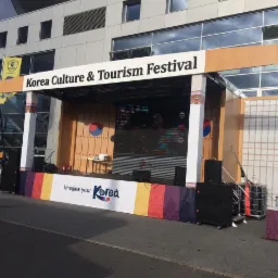 Scena plenerowa z napisem Korea Culture & Tourism Festival, udekorowana w barwy i motywy koreańskie, z widocznym ekranem LED i elementami scenografii nawiązującymi do tradycyjnej architektury...