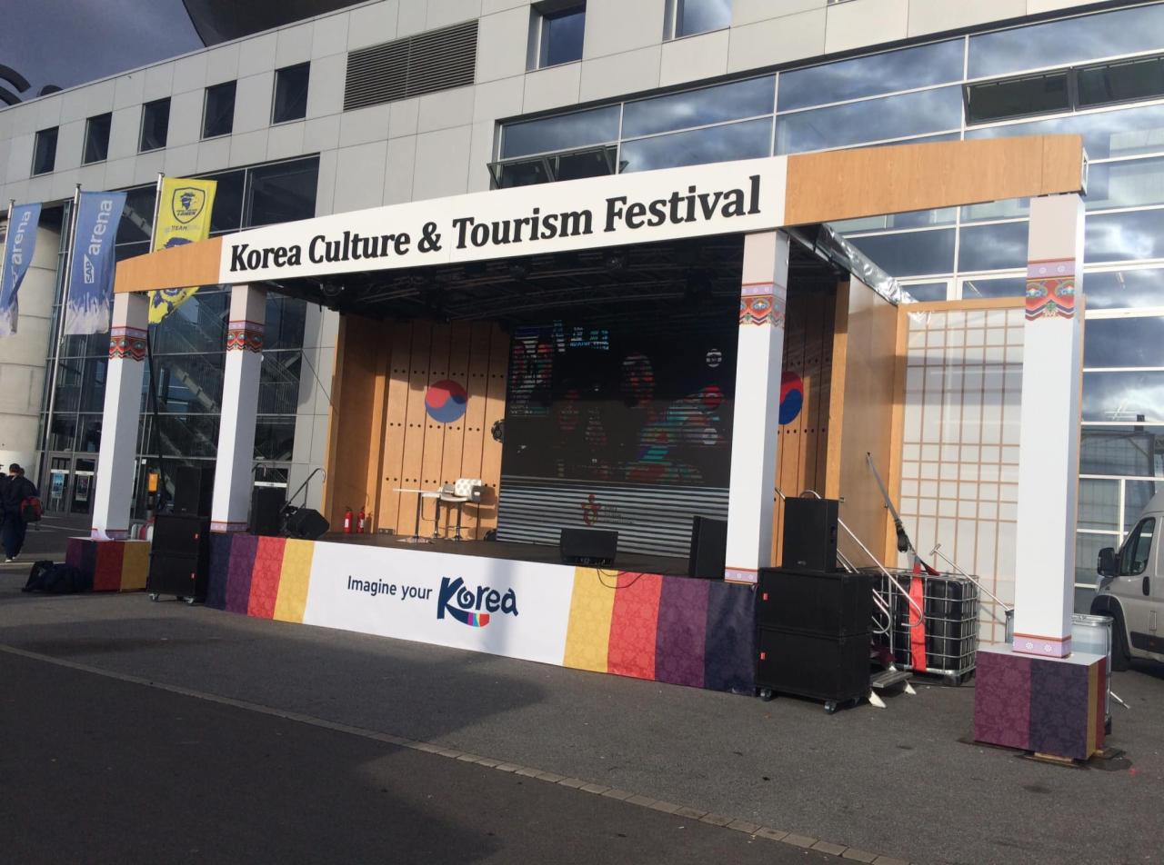 Scena plenerowa z napisem Korea Culture & Tourism Festival, udekorowana w barwy i motywy koreańskie, z widocznym ekranem LED i elementami scenografii nawiązującymi do tradycyjnej architektury...