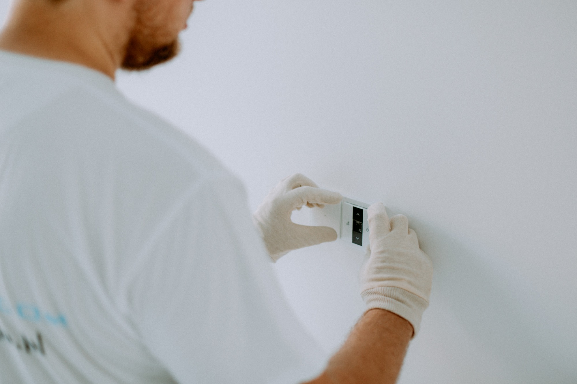Instalator w białych rękawiczkach montuje panel sterowania na białej ścianie; widoczne strzałki góra/dół i przycisk zasilania.