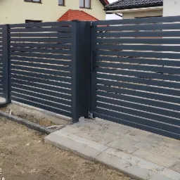 Nowoczesne, poziome, szare przęsła ogrodzenia z bramą przesuwną na posesji z kostką brukową, widok z zewnątrz.