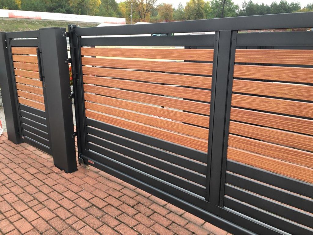 Nowoczesna przesuwna brama wjazdowa z poziomymi panelami drewnopodobnymi i czarną metalową ramą, widoczna na tle kostki brukowej.